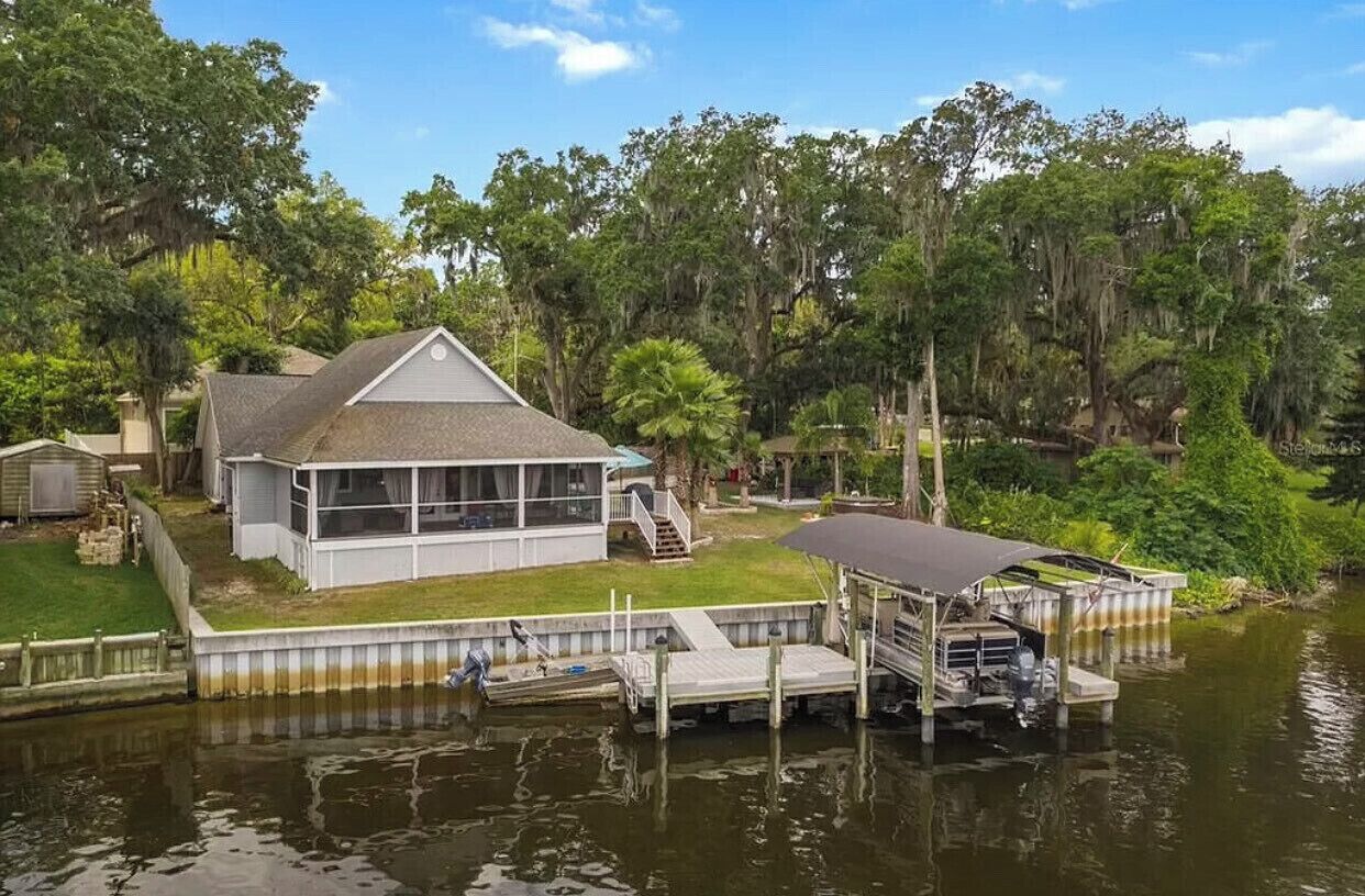 A house with a dock extending into a body of water, surrounded by trees.