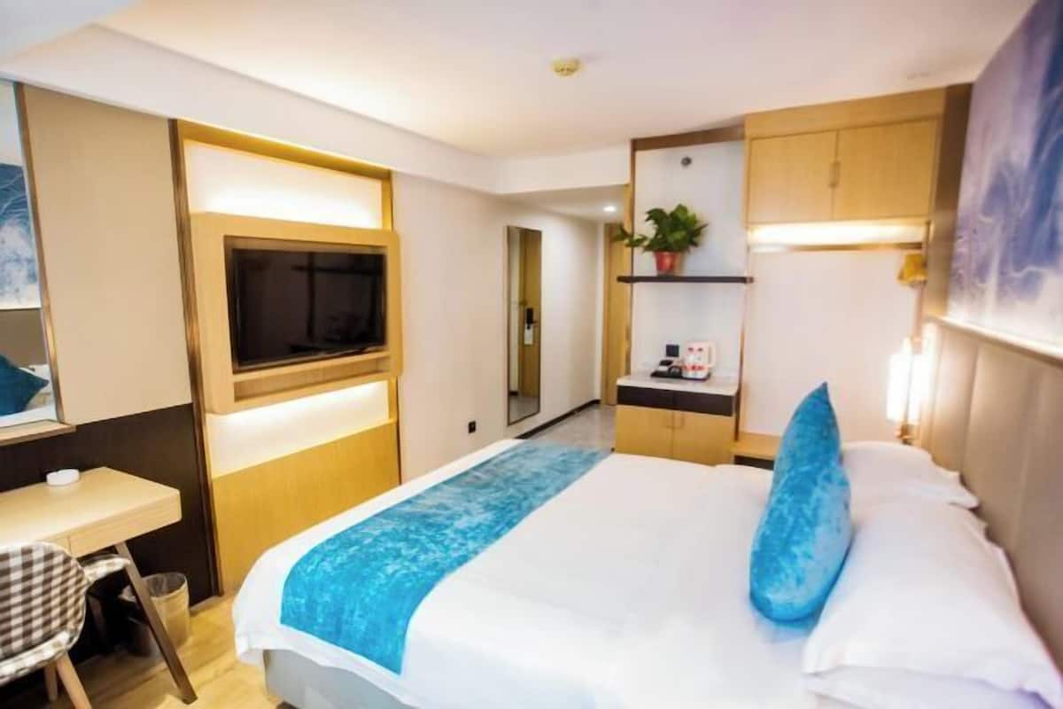 A hotel room with a bed, a desk, a TV, a small kitchenette, and a bathroom.