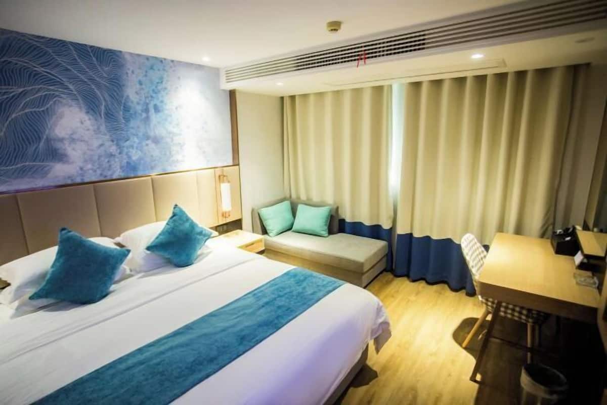 A hotel room with a bed, a sofa, a desk, and a large window with curtains.