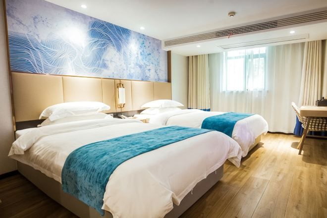 A hotel room with two beds, a desk, a chair, a large abstract painting, and a window with curtains.