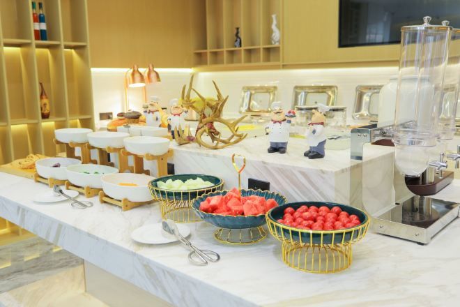 A buffet table with various food items and utensils, including bowls of fruit and a scale.