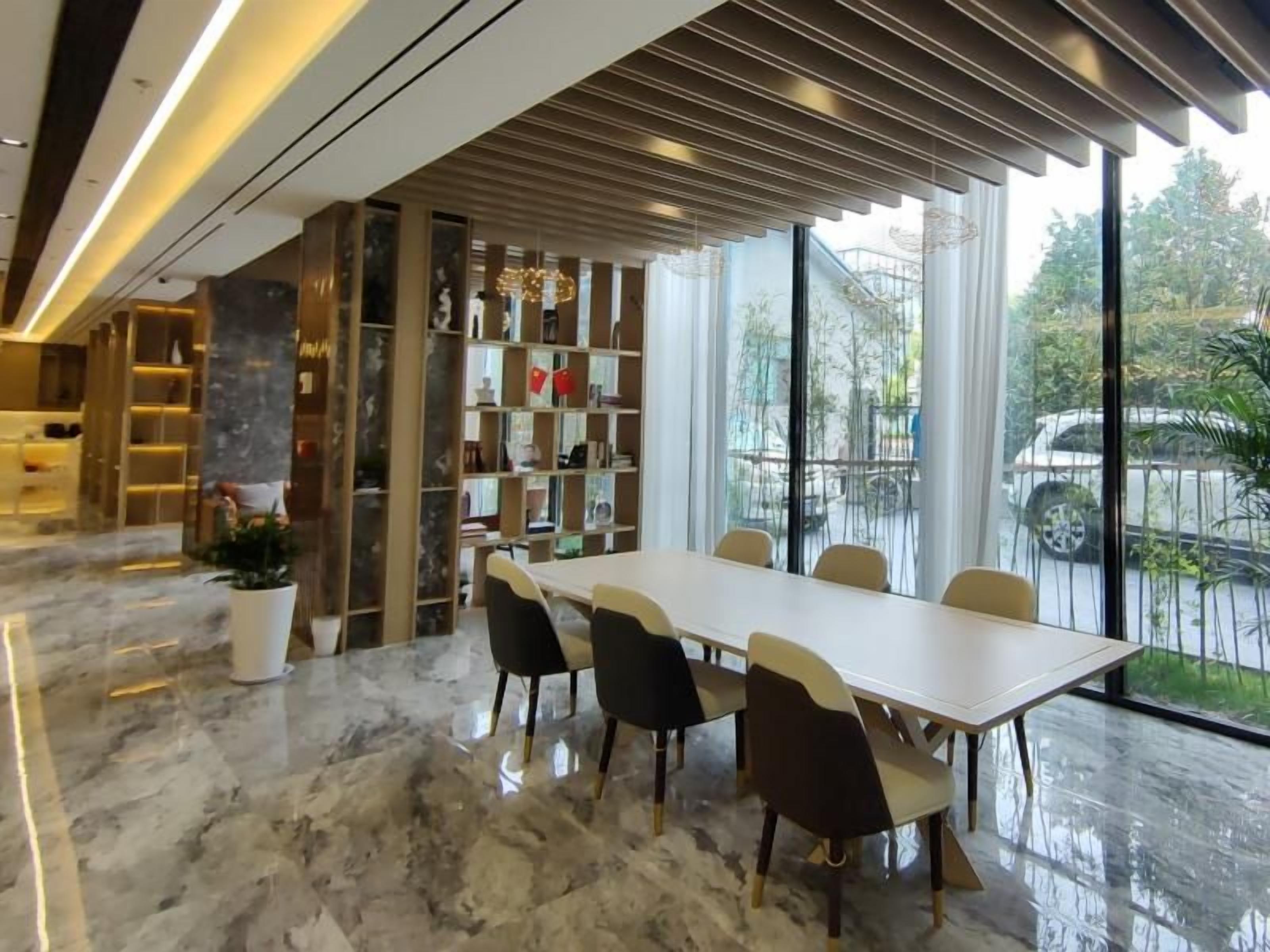 A modern dining area with a marble floor, a long table with chairs, and a bookshelf with various items.