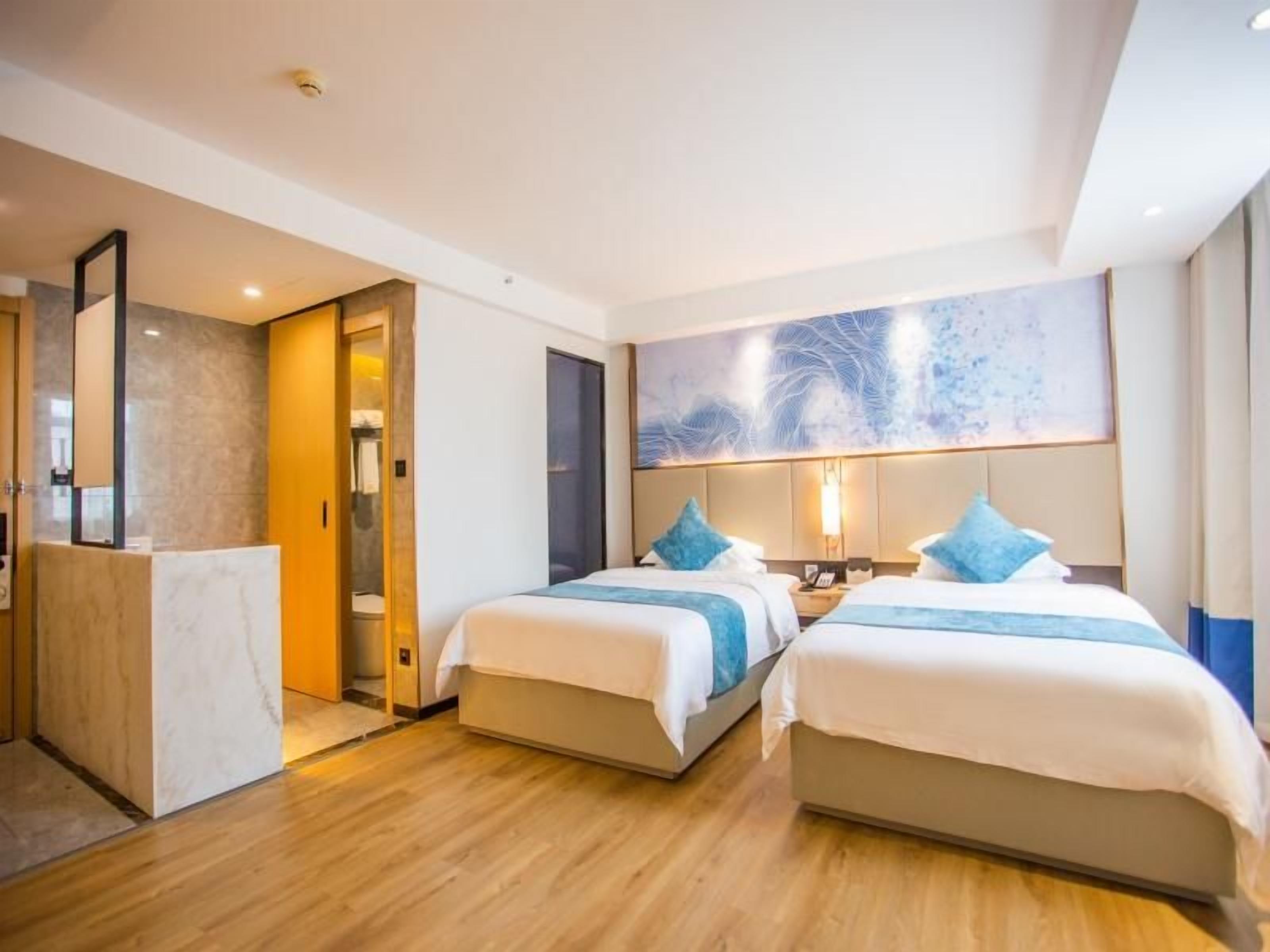 Habitación de hotel con dos camas, un baño y un cuadro abstracto grande en la pared.