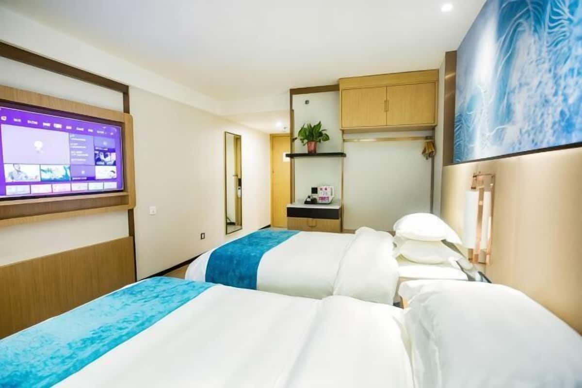 A hotel room with two beds, a TV, a small kitchenette, and a bathroom.