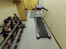 Un gimnasio con cinta de correr, mancuernas y un espejo.