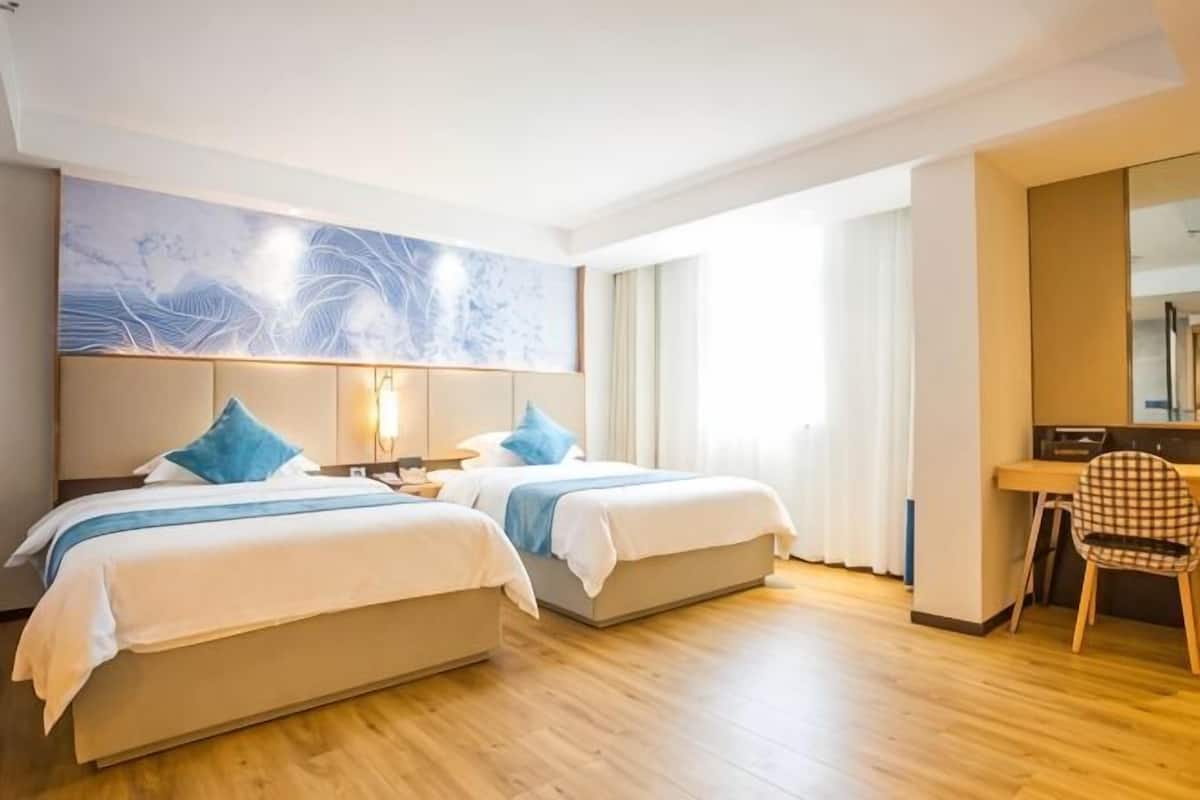 A hotel room with two beds, a desk, a chair, and a large abstract painting on the wall.
