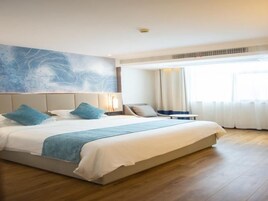 Una habitación de hotel con una cama grande, cabecera con panel decorativo, mesita de noche y ventana con cortinas.