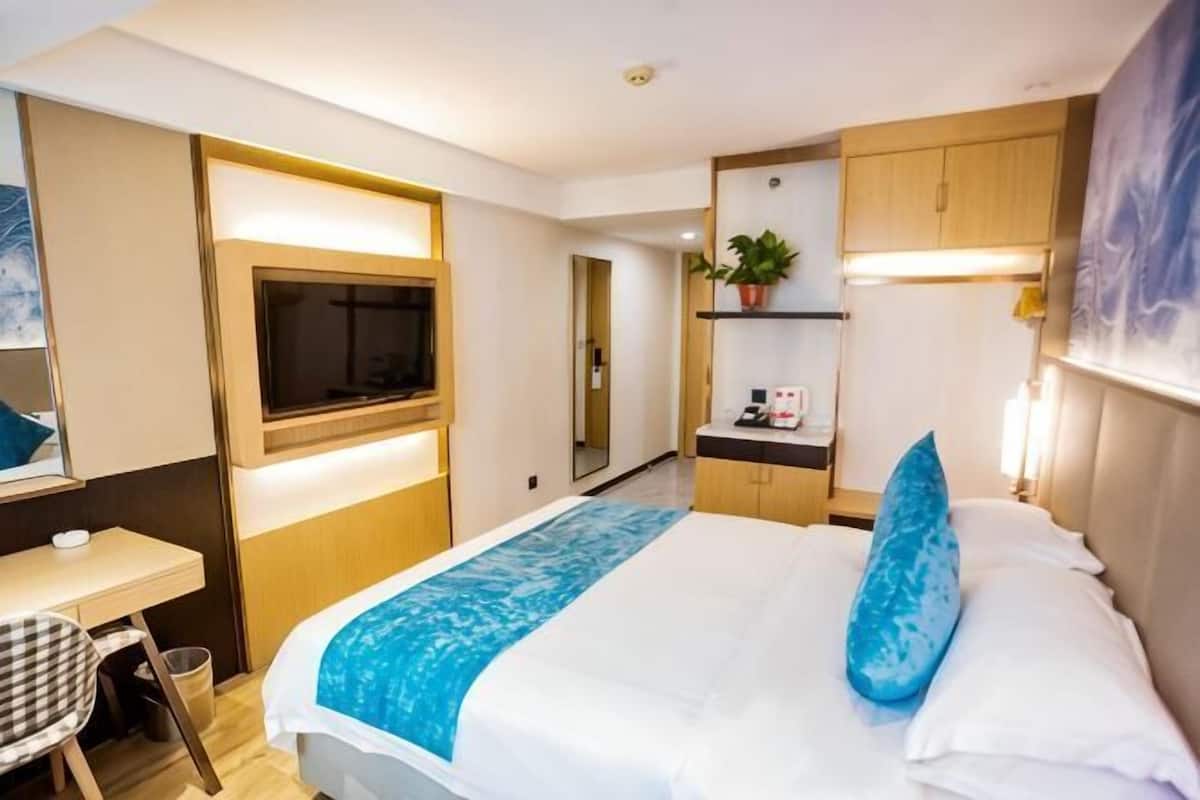 A hotel room with a bed, a desk, a TV, a plant, and a bathroom.
