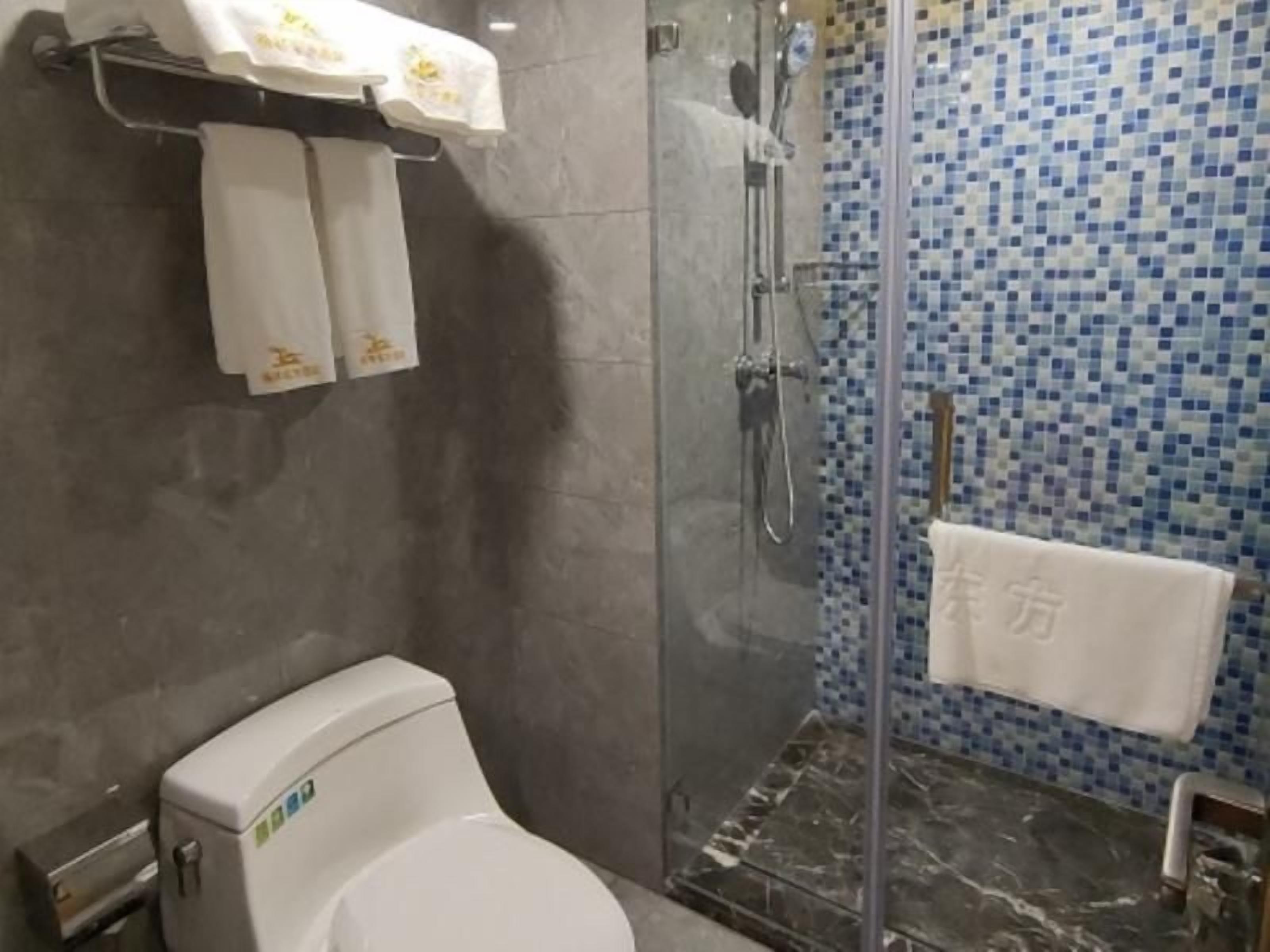 A bathroom with a toilet, a glass-enclosed shower, and a tiled wall.