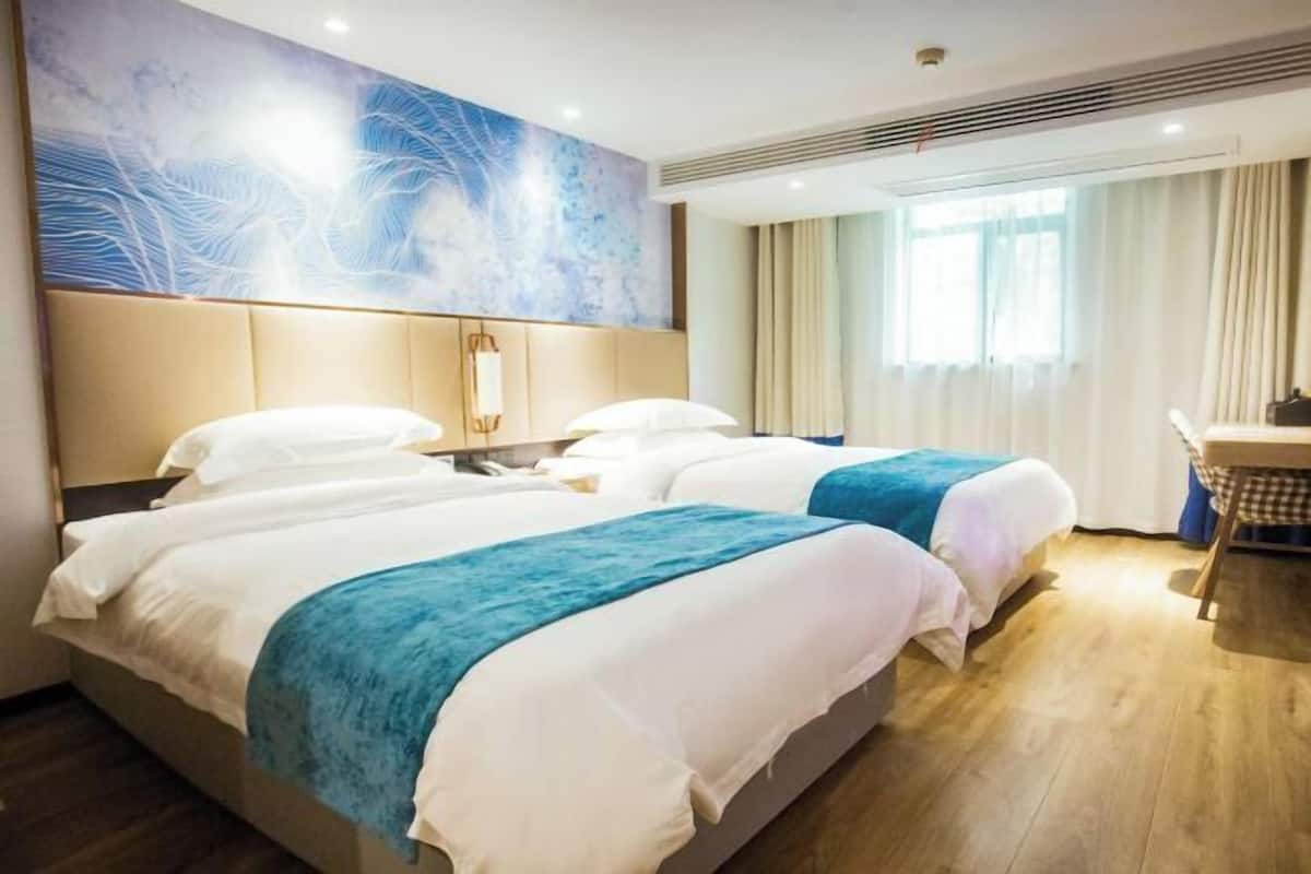 A hotel room with two beds, a large abstract painting on the wall, a desk with a chair, and a window with curtains.