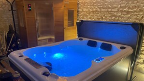 A hot tub with a digital control panel, a wooden cabinet, and a textured stone wall. - Gite Le Travezay avec piscine, sauna et Jacuzzi (Courcoué)