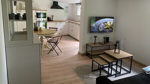 A modern kitchen with white cabinets, a dining area with a round table and chairs, and a TV mounted on the wall. - Gite Le Travezay avec piscine, sauna et Jacuzzi (Courcoué)