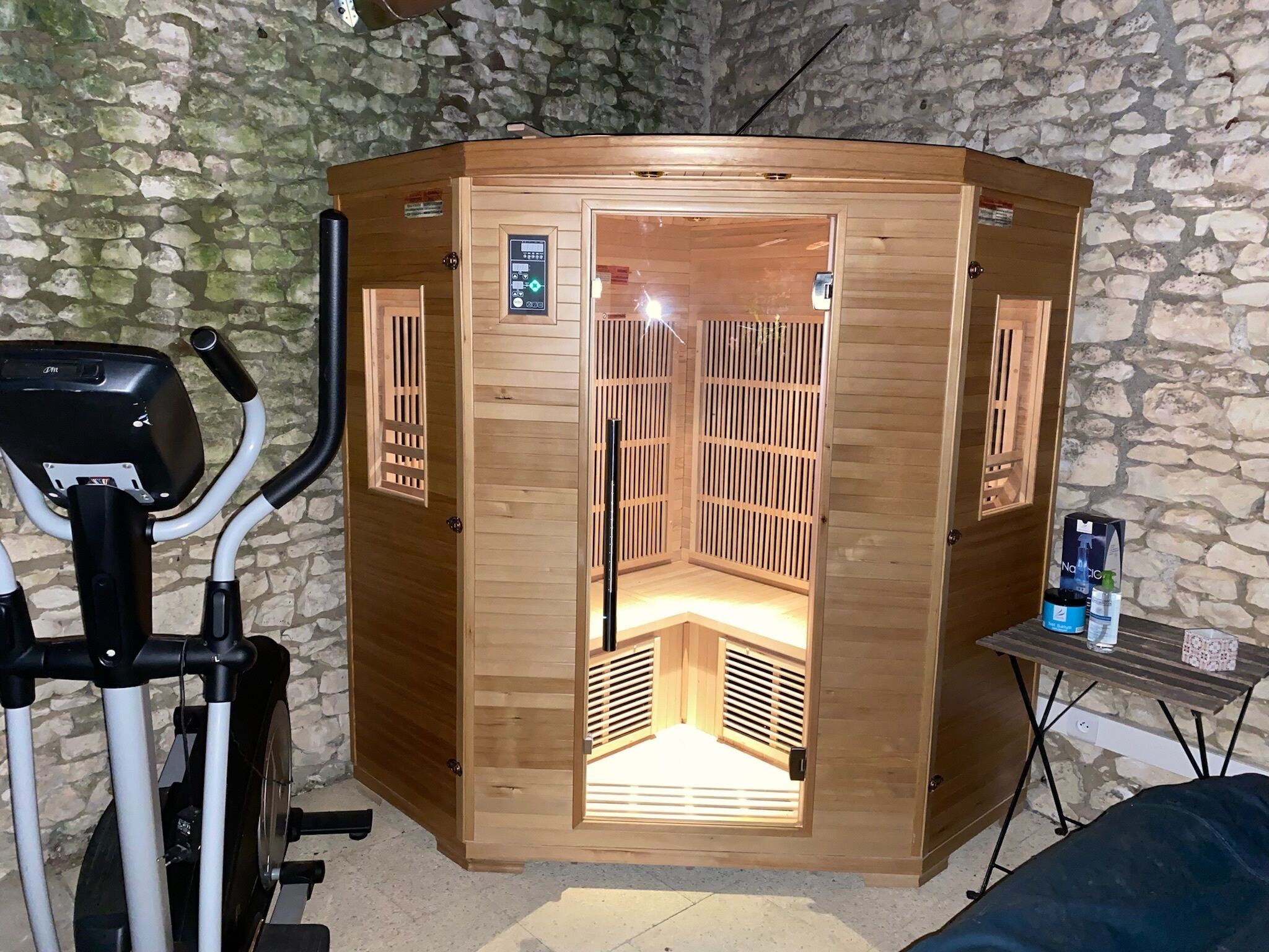 A sauna with a wooden exterior, a control panel, and a small table with items on it.