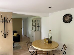 A dining area with a round table, chairs, a cabinet with glass doors, a wall clock, and a coat rack. - Gite Le Travezay avec piscine, sauna et Jacuzzi (Courcoué)
