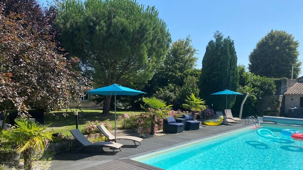 A swimming pool with lounge chairs and umbrellas, surrounded by trees and a wooden deck. - Gite Le Travezay avec piscine, sauna et Jacuzzi (Courcoué)