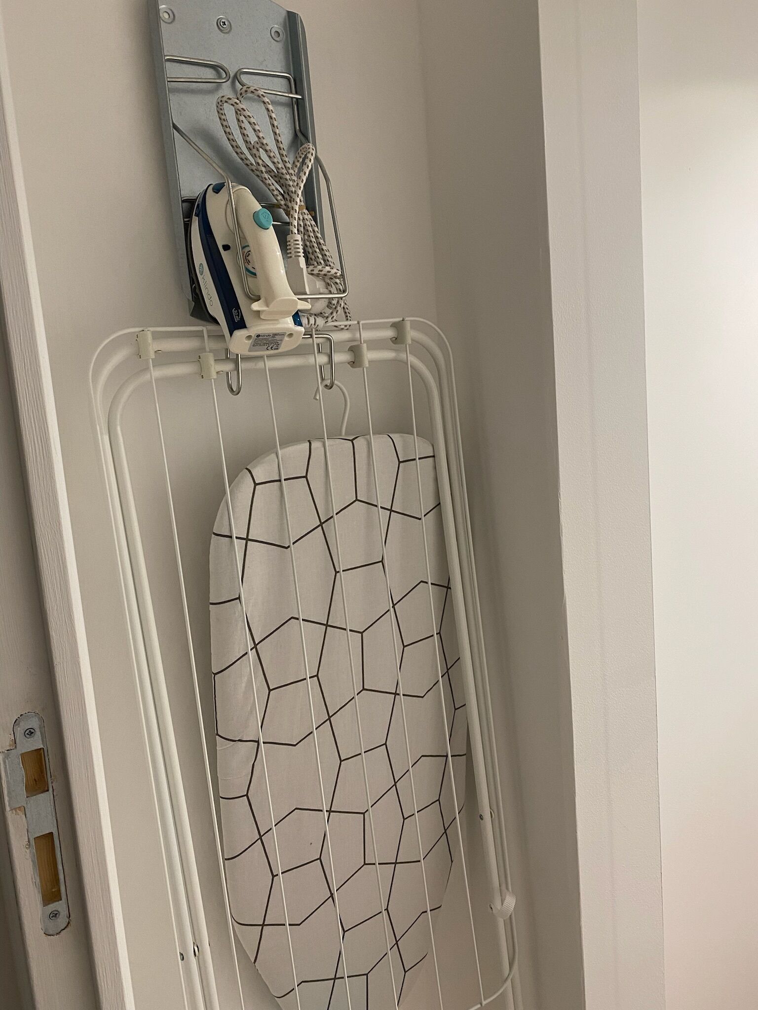 Una puerta blanca con un perchero blanco que sostiene una toalla blanca y un secador de pelo blanco.