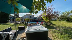 A hot tub in a backyard with a pool, outdoor furniture, and a house in the background. - Gite Le Travezay avec piscine, sauna et Jacuzzi (Courcoué)
