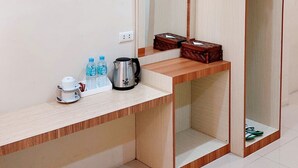 A compact room with a flat-screen TV mounted on the wall, a wooden bench with a cup and water bottles, and a mirror cabinet with a hanging rack. - Hotel Amel Convention Hall (Banda Aceh)