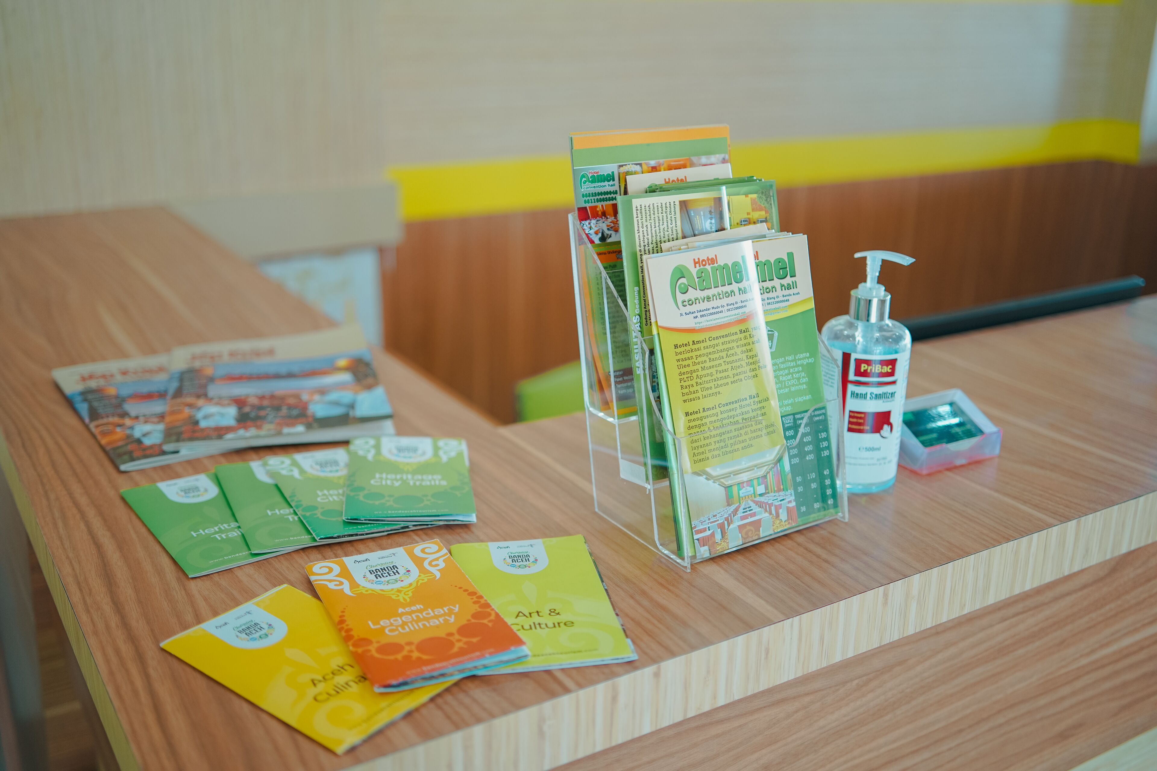 Un mostrador de recepción de madera con folletos, dispensador de gel antibacterial y caja de pañuelos.