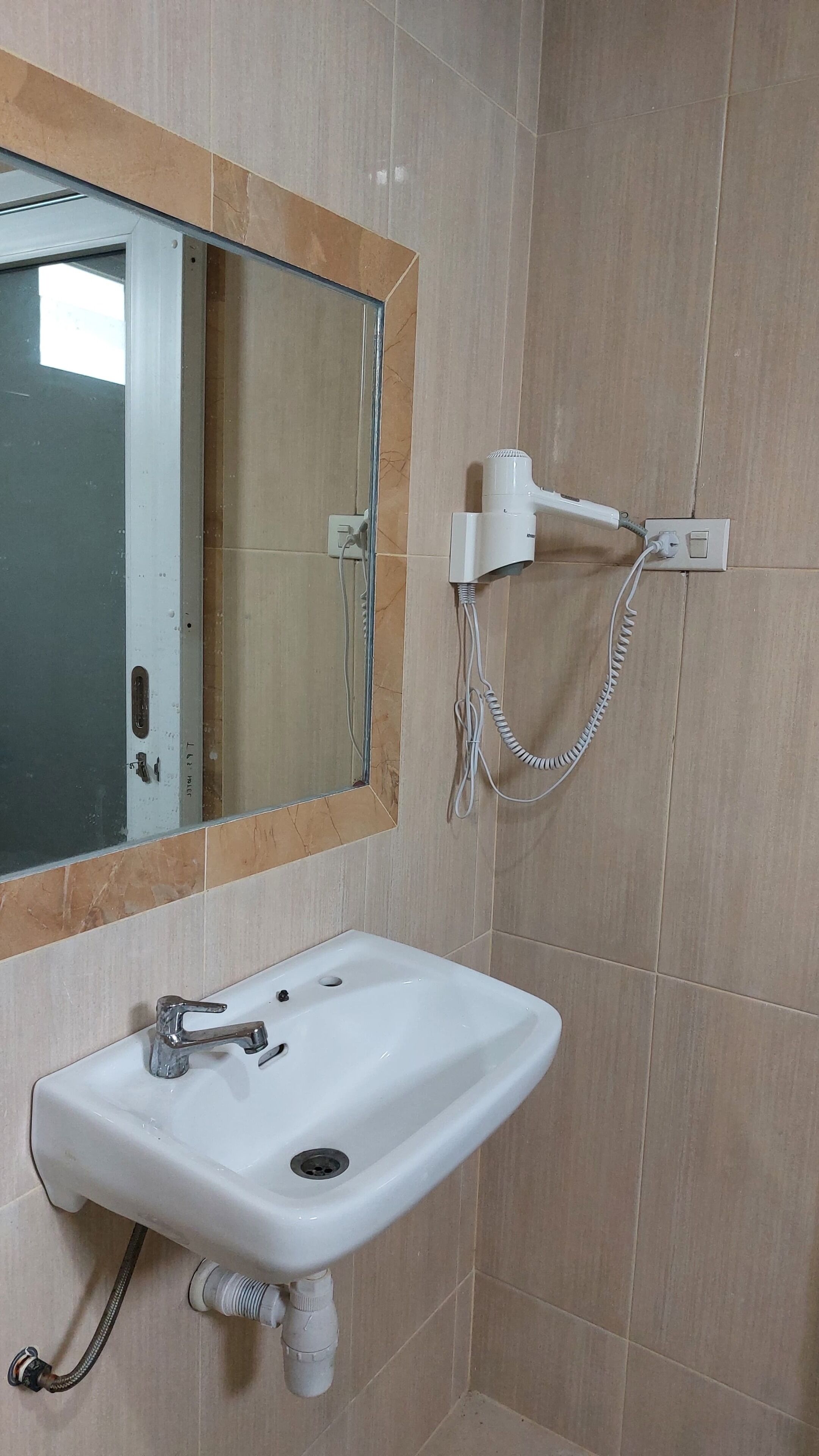 A bathroom with a white sink, a mirror with a wooden frame, and a hairdryer mounted on the wall.