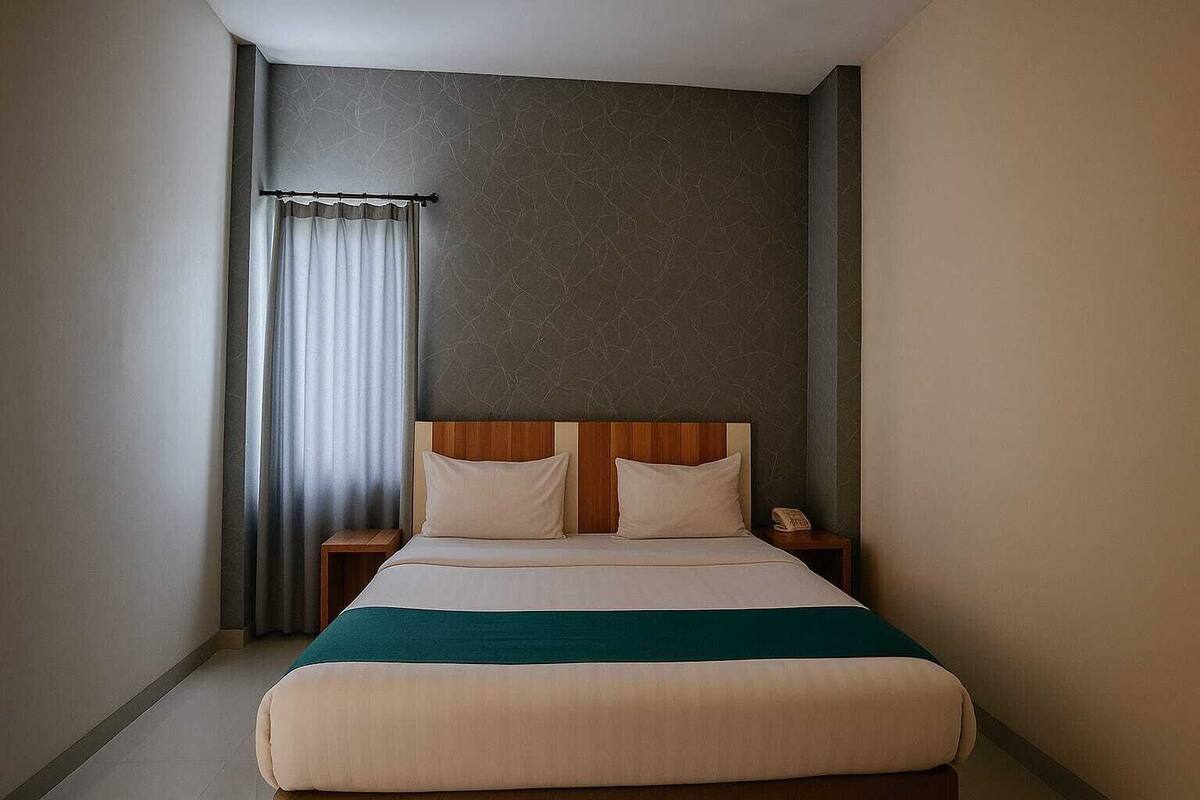 A hotel room with a bed, a nightstand, a telephone, and a curtain.