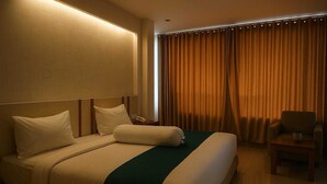 A hotel room with a large bed, a bedside table with a lamp, a chair, and a window with curtains. - Hotel Amel Convention Hall (Banda Aceh)