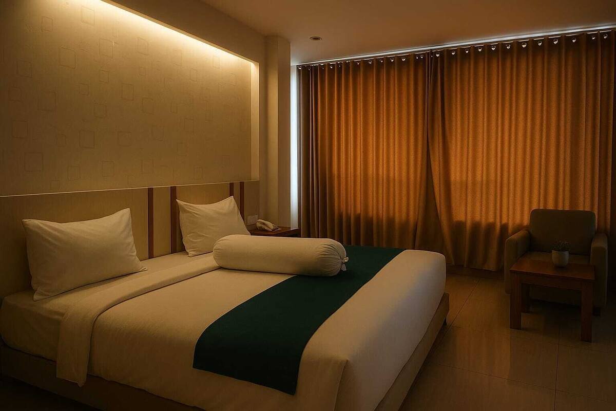 A hotel room with a large bed, a bedside table with a lamp, a chair, and a window with curtains.