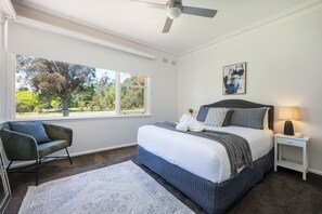 A bedroom with a large window, a bed with a dark headboard, a bedside table with a lamp, and a chair. - Bancroft House Mudgee by Your Innkeeper (Mudgee)