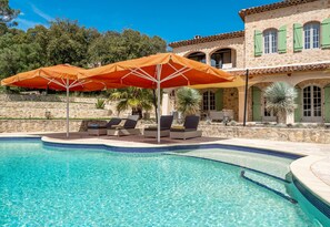 A swimming pool with lounge chairs and umbrellas, surrounded by stone walls and a building with green shutters. - Mas de l'Aven – Dream villa with heatable pool within walking distance of Lorgues (Lorgues)
