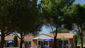 Ein Gebäude mit rotem Ziegeldach, Außenbereich mit blauen Sonnenschirmen und umliegenden Bäumen.