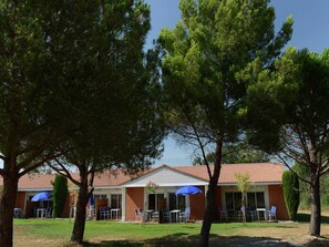 A building with a red-tiled roof, outdoor seating with blue umbrellas, and surrounding trees. - Romantic Vineyard Getaway (Sallèles-d'Aude)