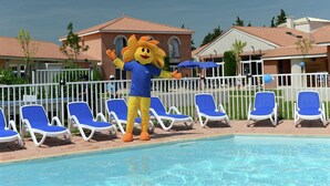 Eine Maskotte an einem Pool mit Liegestühlen und einem Gebäude im Hintergrund.