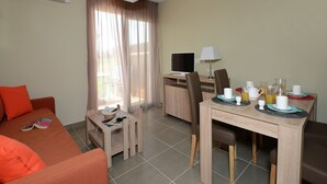 Ein Hotelzimmer mit einer Sitzecke, einem Esstisch mit Stühlen, einem Fernseher und einem Fenster mit Vorhängen.
