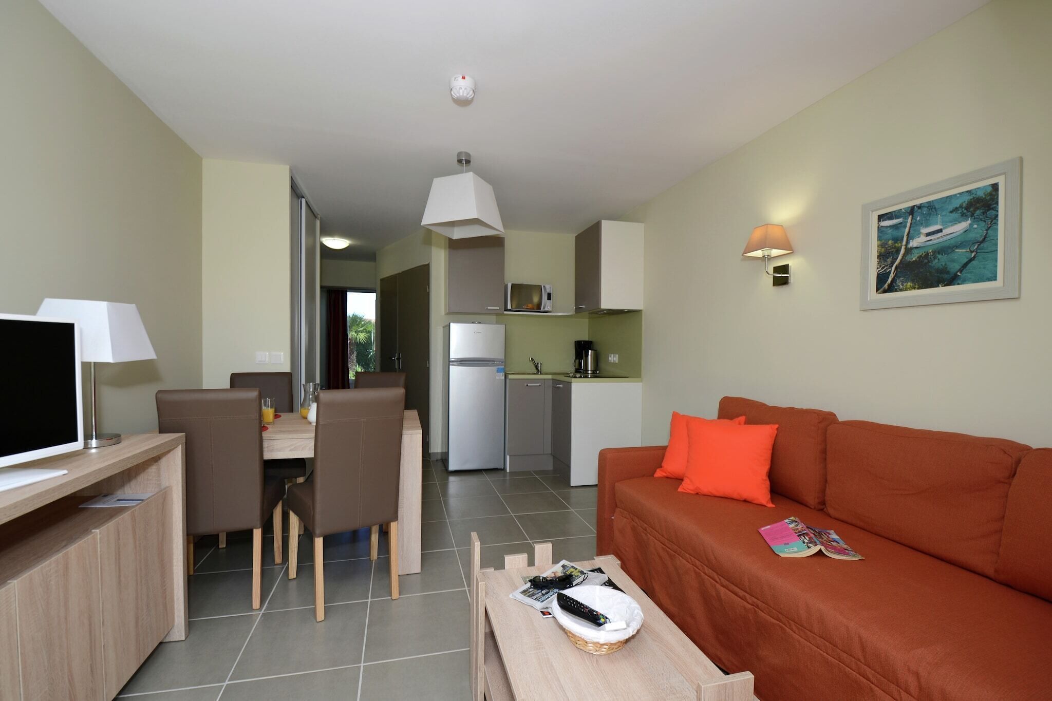 Een knus woongedeelte met een eethoek, kitchenette en een bank met een tijdschrift.