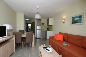 A compact living space with a dining area, kitchenette, and a sofa with a magazine. - Family-Friendly Apartment (Sallèles-d'Aude)