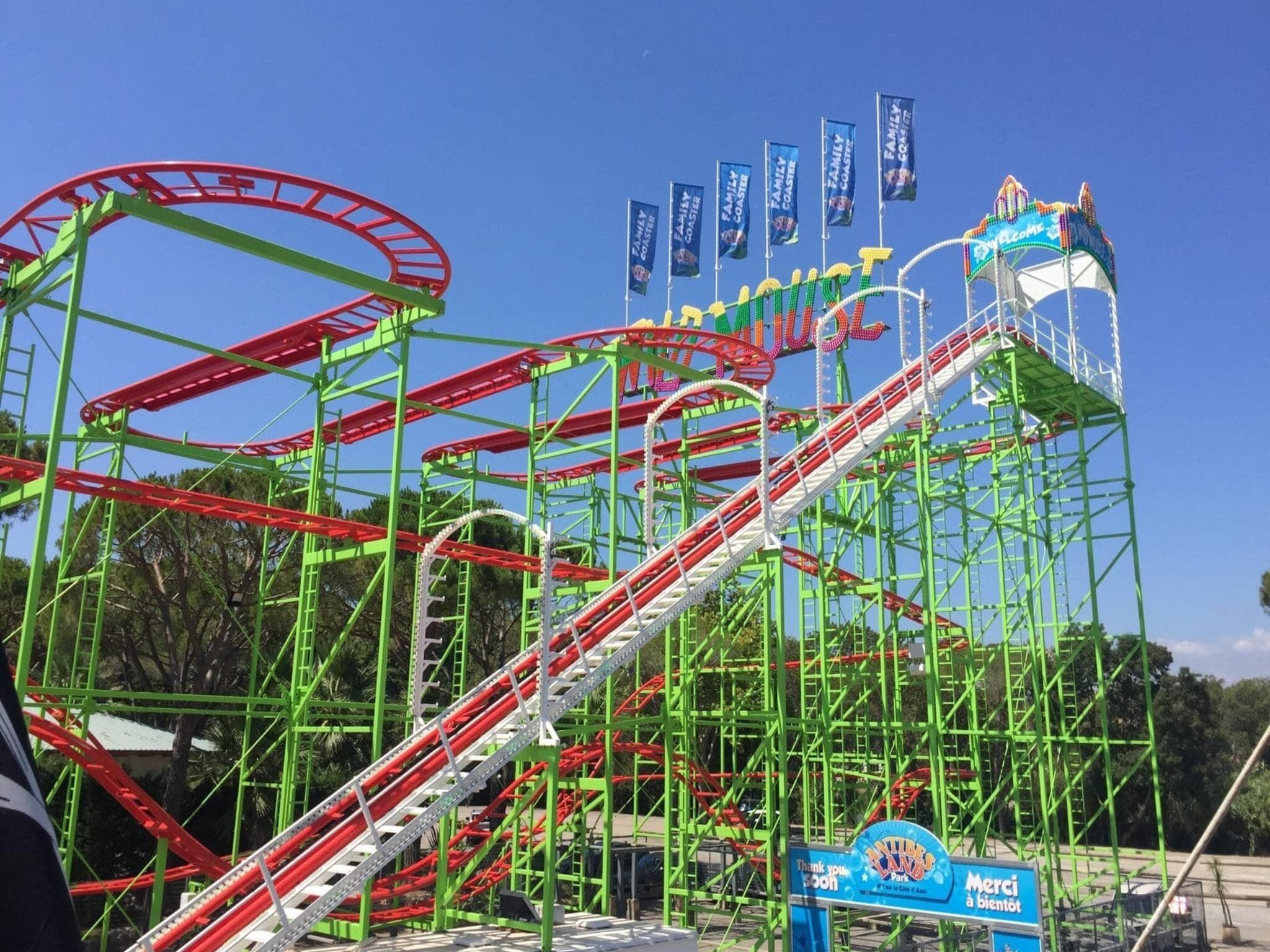 A roller coaster with a steep drop and multiple loops, surrounded by green metal structures and flags.