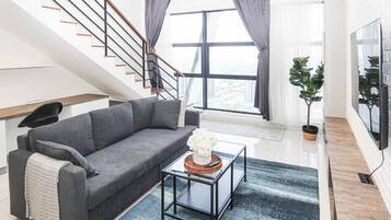 A modern living room with a grey sofa, a coffee table with a decorative item, a staircase with black railings, and a large window with curtains.