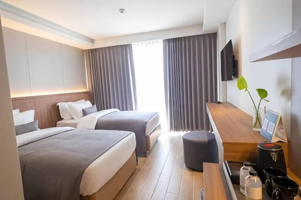 Een hotelkamer met twee bedden, een bureau, een televisie en een raam met gordijnen.