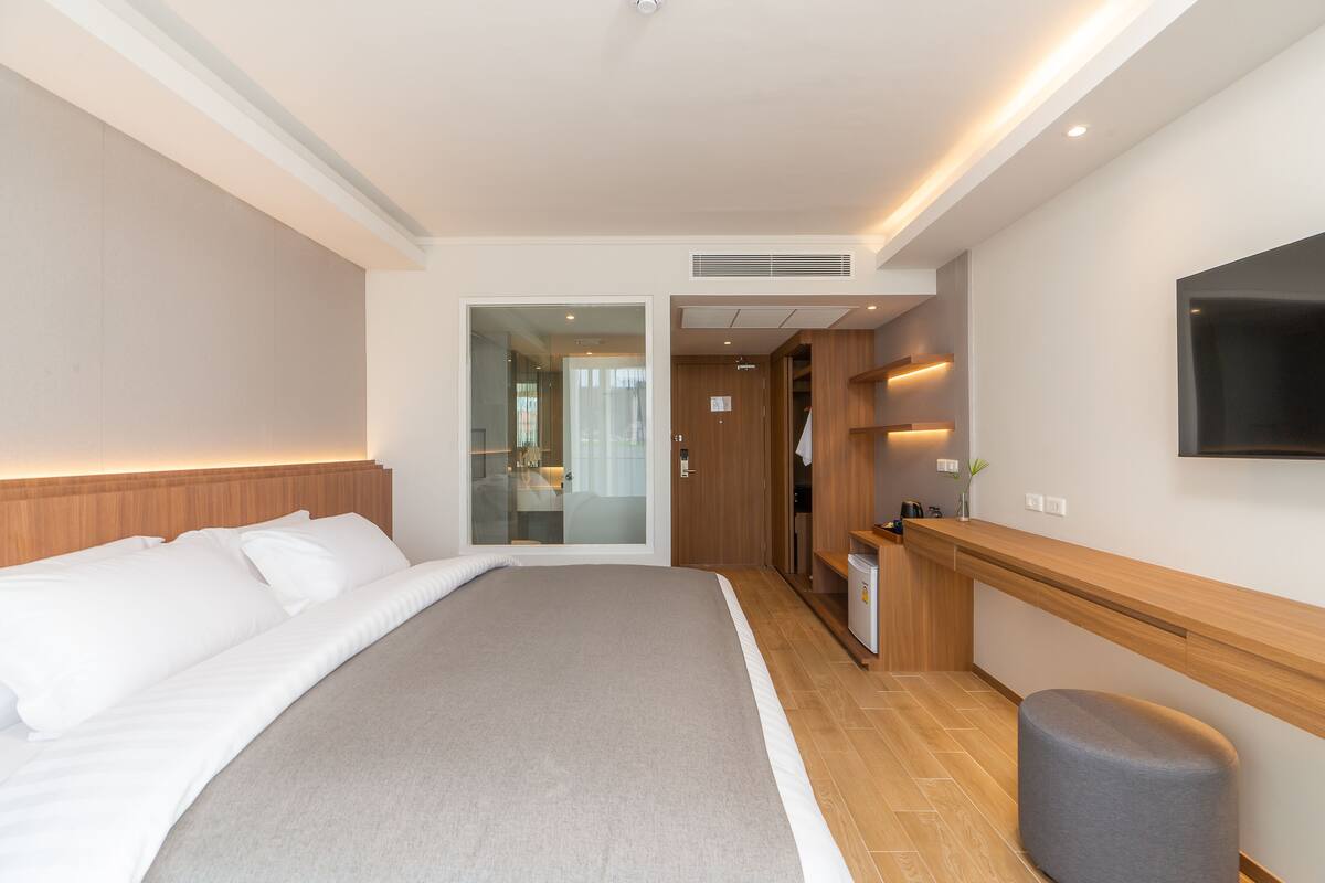 Een moderne hotelkamer met een groot bed, een houten hoofdbord, een flatscreen televisie aan de muur en een zithoekje.