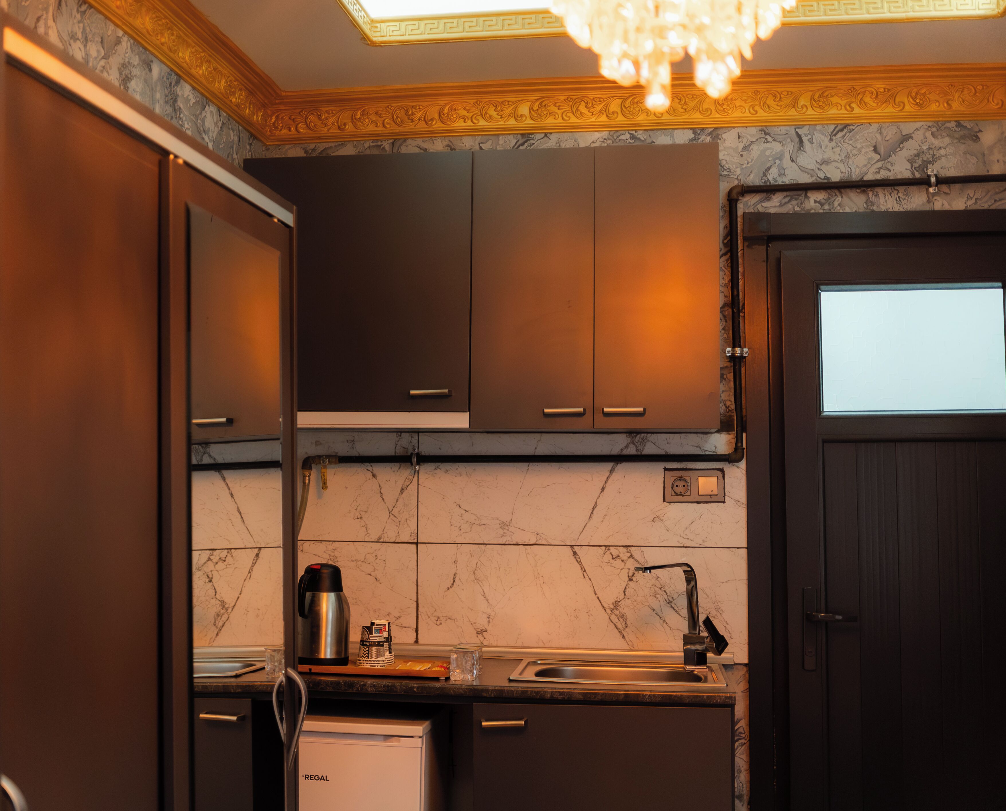 A kitchen with dark cabinets, a marble backsplash, a built-in oven, and a sink.