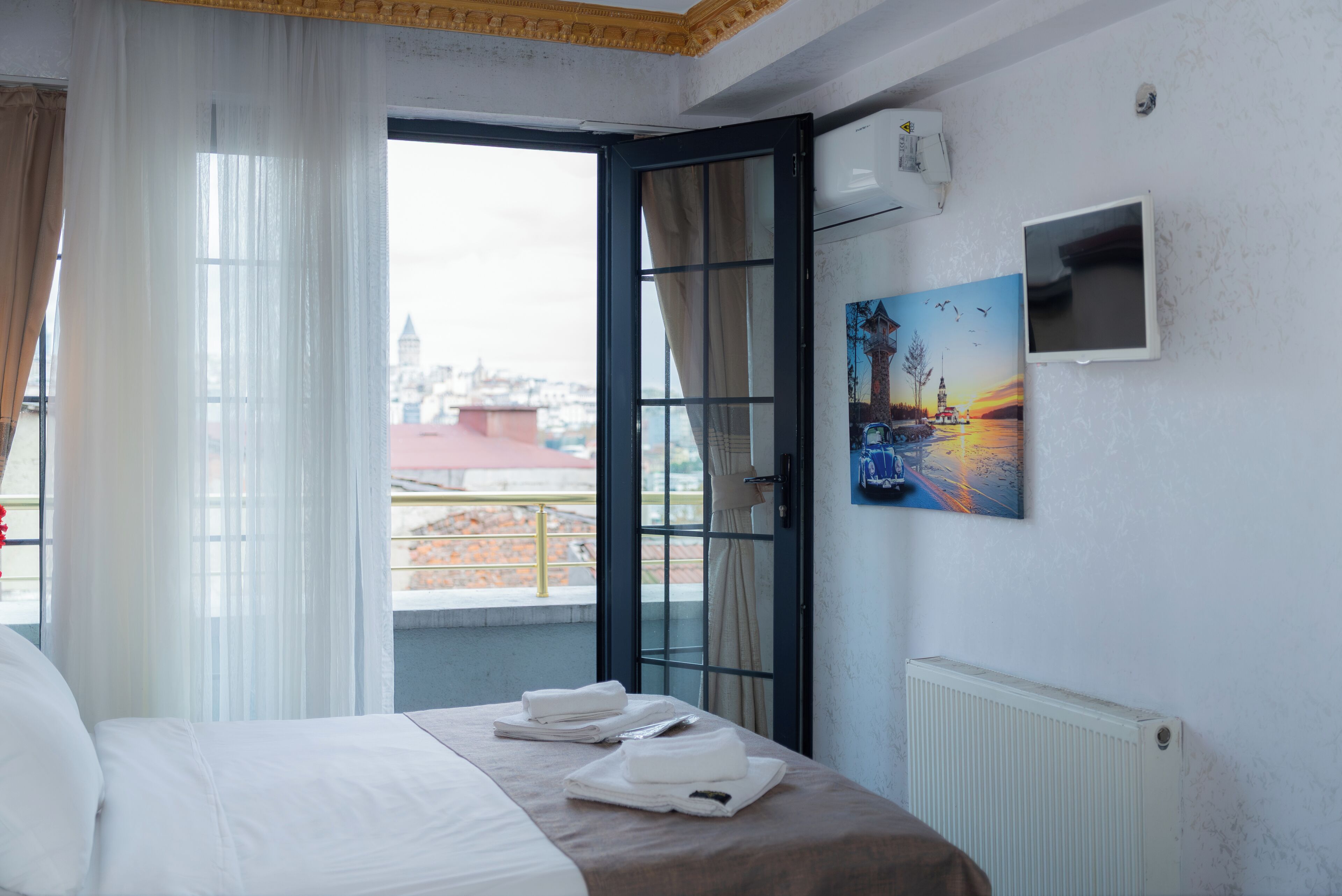 Een hotelkamer met een bed, een schilderij, een raam met gordijnen en uitzicht op de stad.