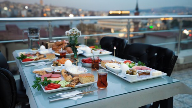 Een tafel gedekt met diverse gerechten en een theeglas, met uitzicht op een stadsgezicht.