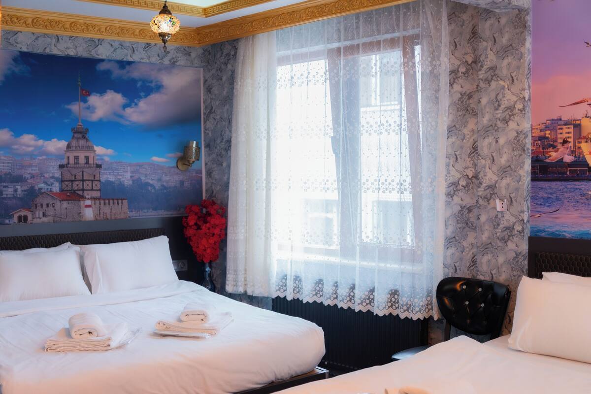 A hotel room with a bed, a chair, a window with sheer curtains, and a wall mural.