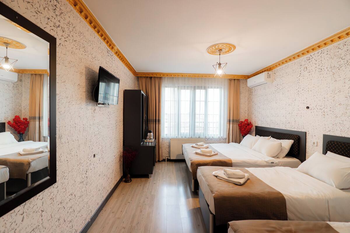 A hotel room with two beds, a TV, a mirror, and a window with curtains.