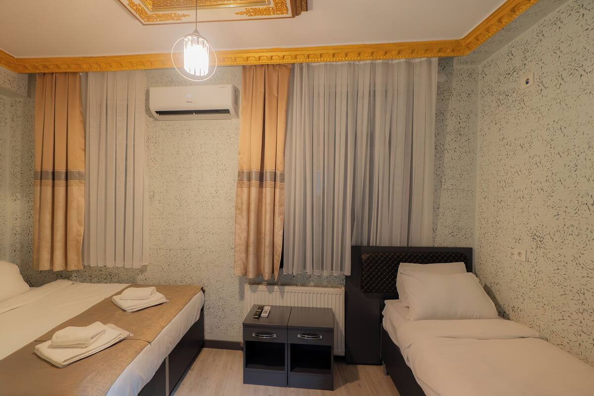 A hotel room with two beds, a small table, a nightstand, and an air conditioning unit.