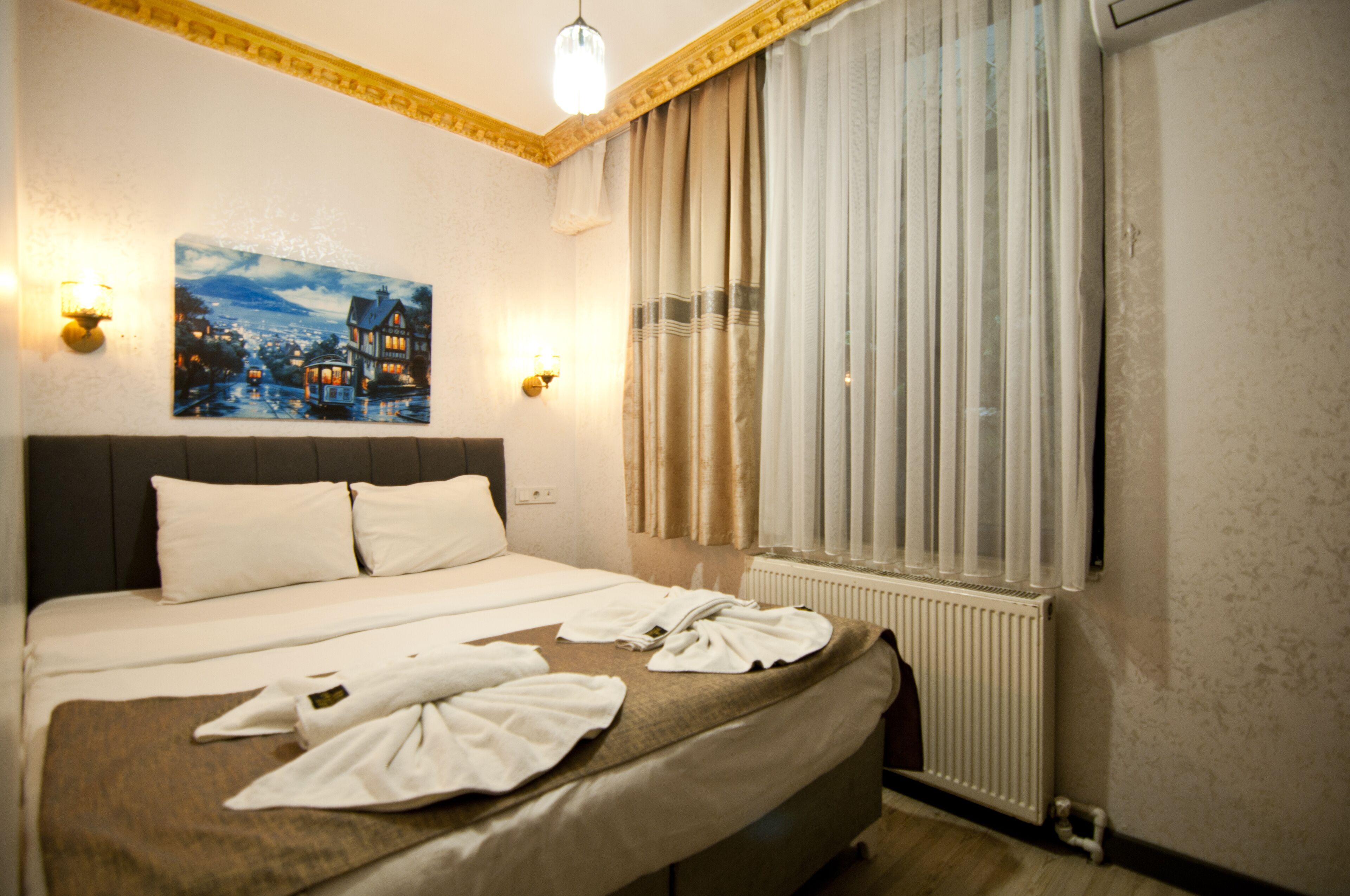 Una habitació d'hotel amb un llit, un quadre a la paret i una finestra amb cortines.