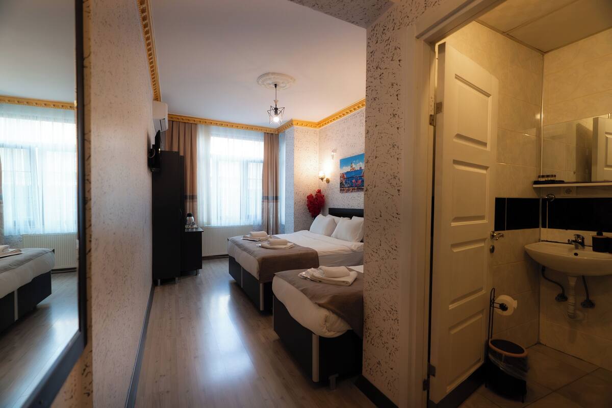 A hotel room with two beds, a bathroom with a sink, and a large mirror.