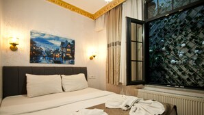 Hotelkamer met een bed, twee wandlampen, een schilderij, een raam met uitzicht op groen en een radiator.
