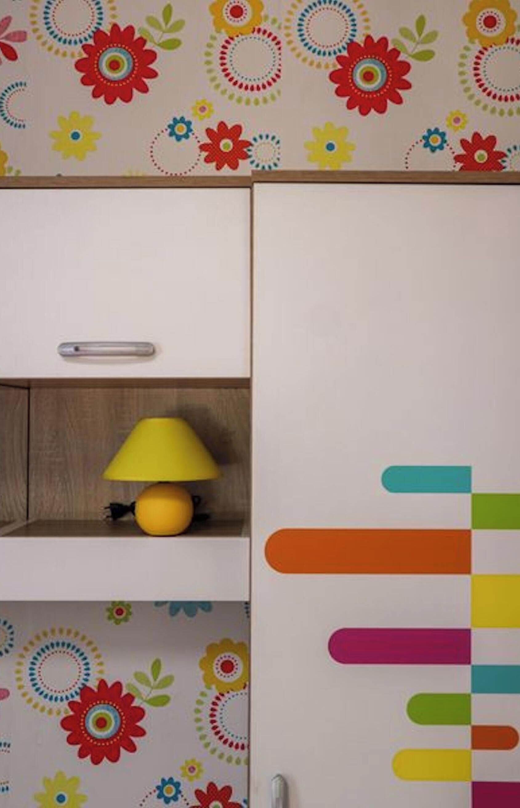 A room with a wooden cabinet, a yellow lamp, and a wall with colorful circular patterns.