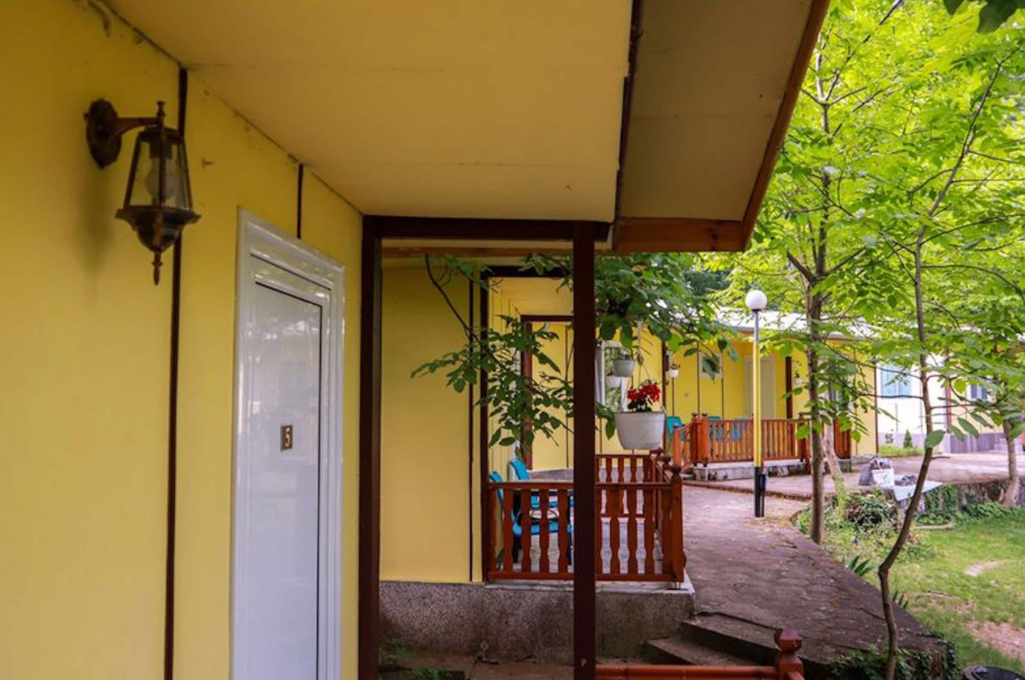 A yellow building with a white door, a wooden porch, and a small garden area.